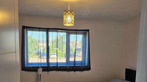 Un dormitorio con una cama, un calentador portátil, una ventana con cortinas y una lámpara en el techo.