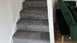 Una escalera con peldaños alfombrados, un sofá verde y un espejo redondo pequeño en la pared.