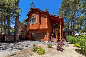 A two-story wooden cabin with a garage, surrounded by tall trees and a landscaped yard. - Garden Mountain Home (South Lake Tahoe)