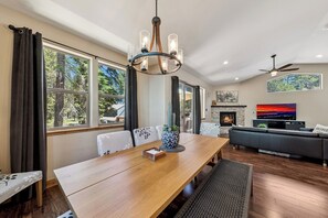 Uma sala de jantar com mesa de madeira, cadeiras, um candelabro e uma lareira.