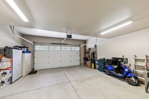 Eine Garage mit einer weißen Tür, einem blauen Roller und verschiedenen Werkzeugen und Geräten.