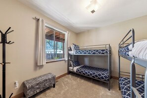 Quarto com beliche, um cabideiro, um banco e uma janela com cortinas.