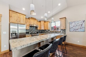 Una cocina moderna con gabinetes de madera, electrodomésticos de acero inoxidable, encimera de granito y taburetes de bar.