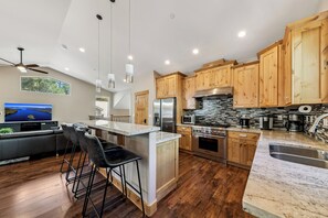 A modern kitchen with wooden cabinets, a large island, bar stools, and a built-in TV. - Garden Mountain Home (South Lake Tahoe)