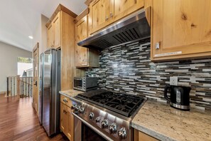 A modern kitchen with wooden cabinets, a stainless steel stove, a microwave, and a tiled backsplash. - Garden Mountain Home (South Lake Tahoe)