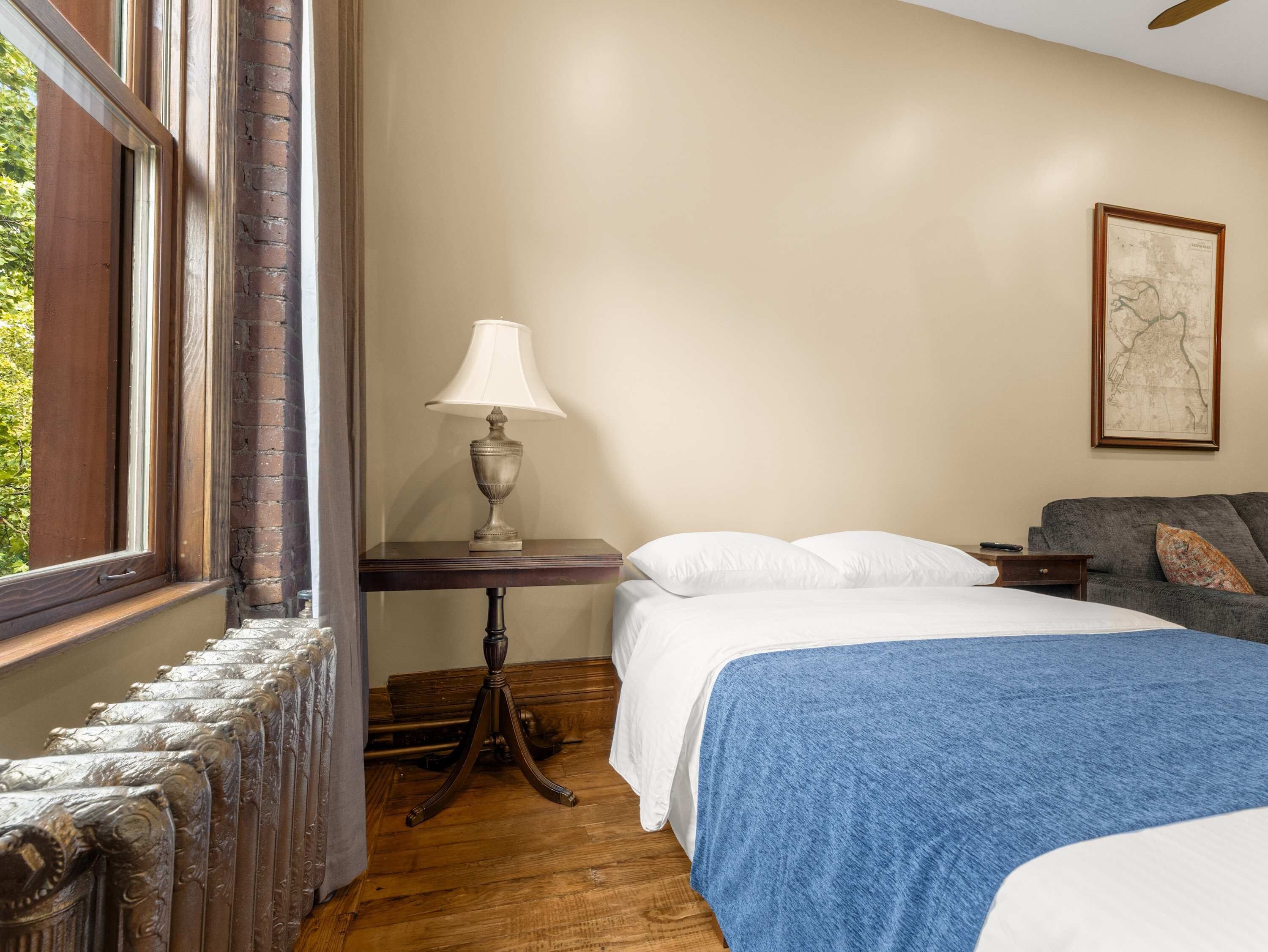 Une chambre à coucher avec un lit, une table de chevet, une lampe, une fenêtre et une carte accrochée au mur.