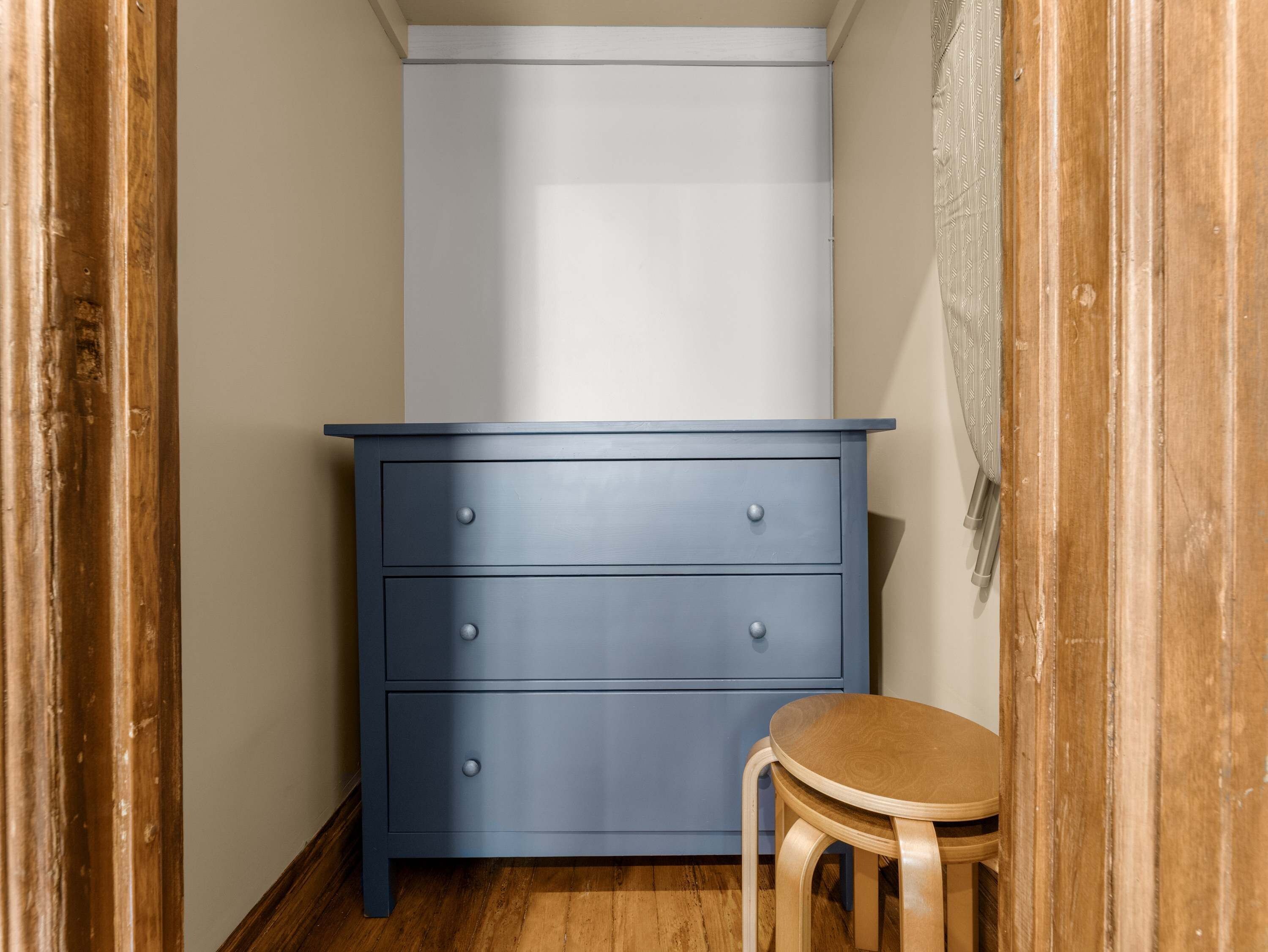Une petite pièce avec une commode bleue, une chaise en bois et un meuble blanc.