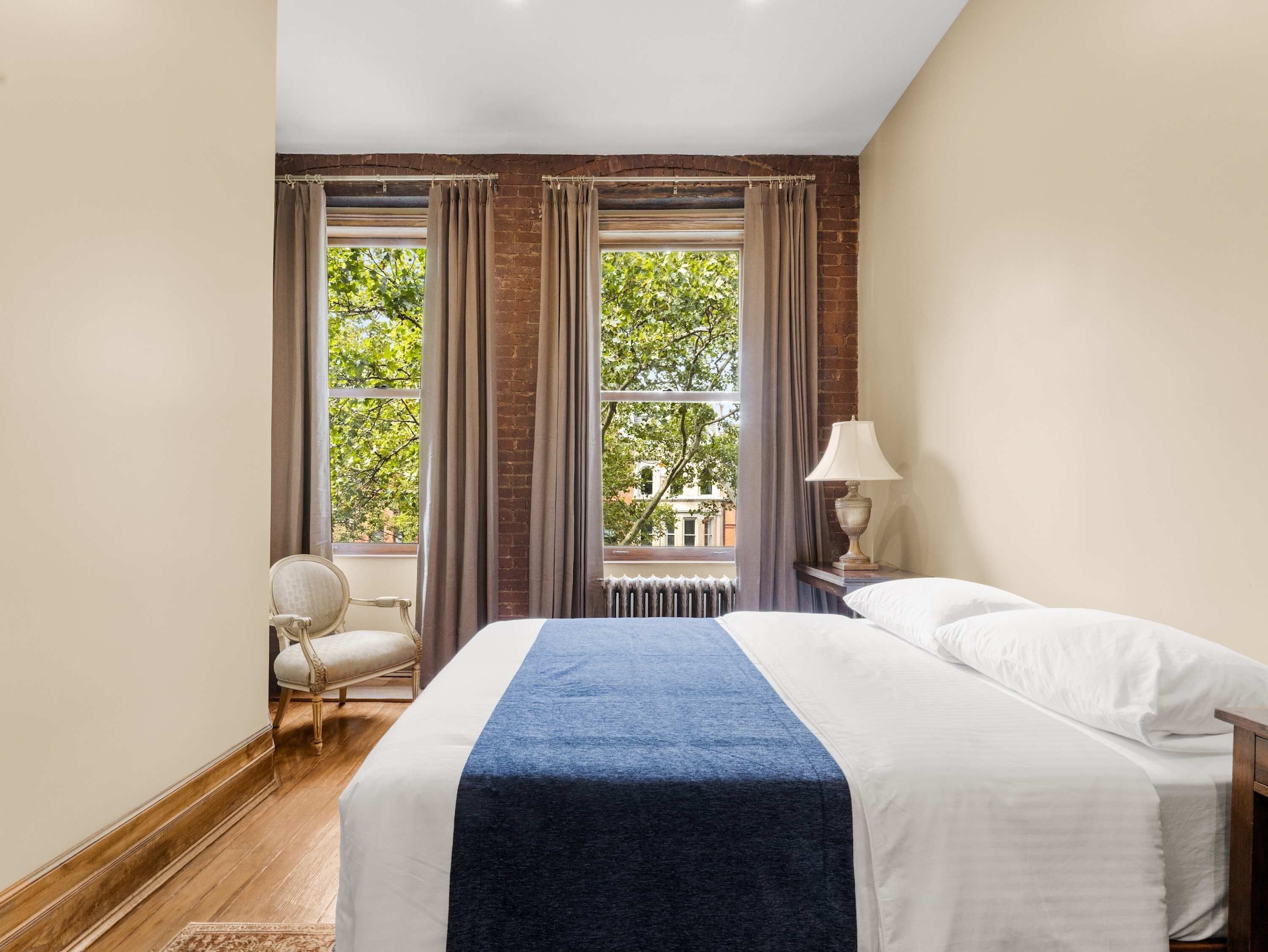A hotel room with a bed, a chair, a lamp, and a view of trees through the window.