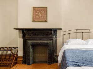 A bedroom with a bed, a wooden side table, a fireplace, and a framed picture on the wall. - Hamilton House Apt 5 with Pvt Bath & Fireplace (New York)