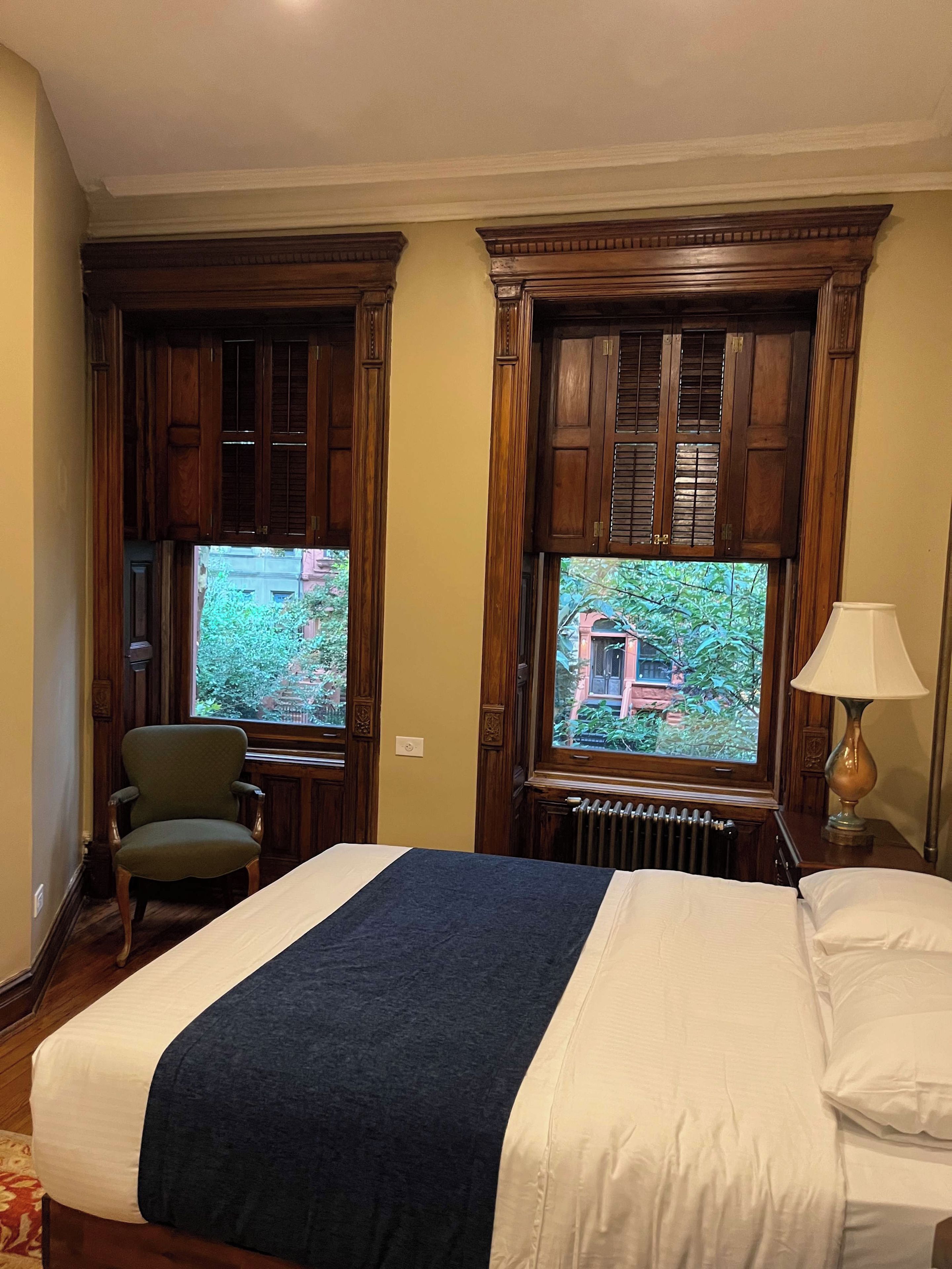 A hotel room with a bed, a chair, a desk, and a view of greenery outside.