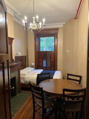 Una habitación con cama, una mesa de comedor con sillas, una araña y vistas al exterior por una ventana.
