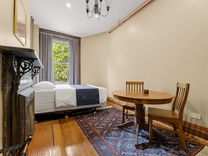 A room with a bed, a round wooden table with two chairs, a patterned rug, and a chandelier.