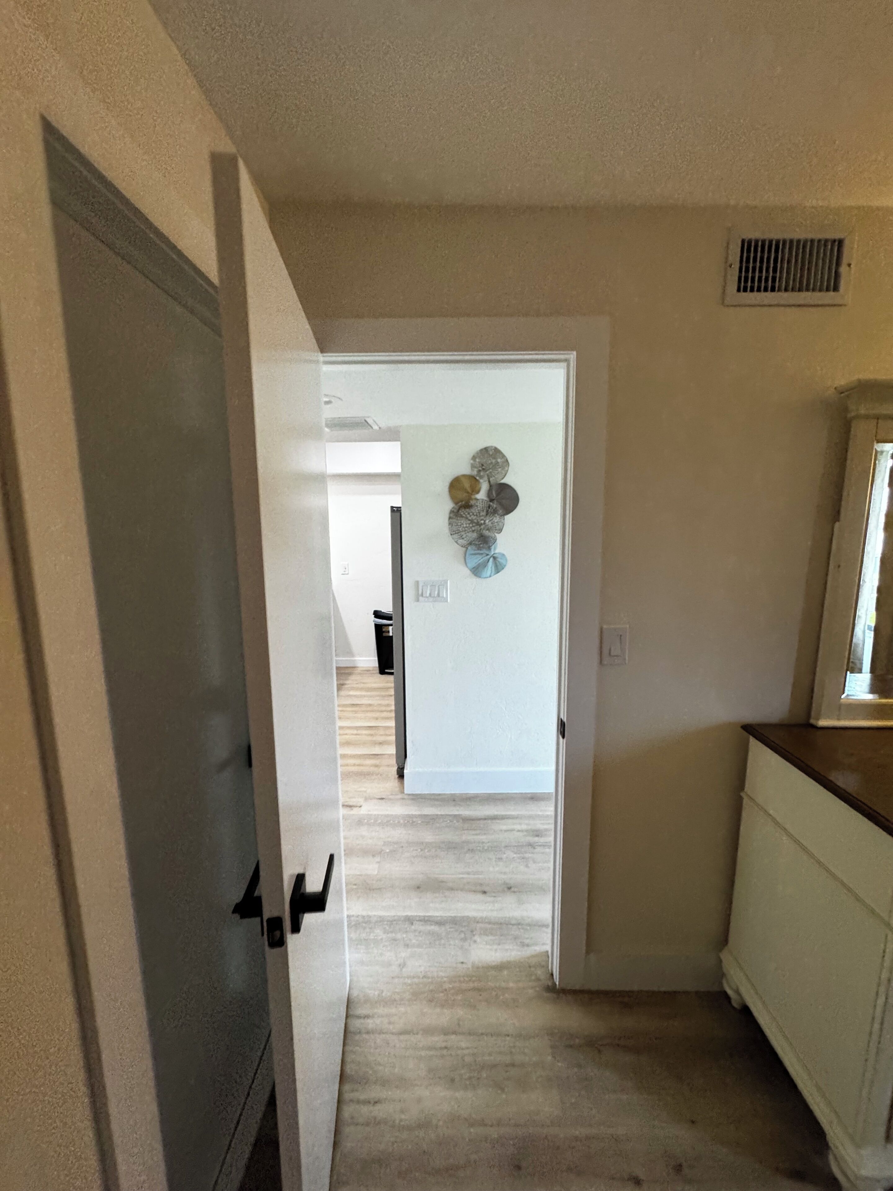 A hallway with a white door, a vent on the wall, and a light switch.