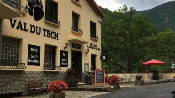 A building with a sign reading 'VAL DU TECH' and 'Hotel Bed & Breakfast.' There are outdoor seating areas with umbrellas. - Hotel Val Du Tech  (Prats-de-Mollo-la-Preste)