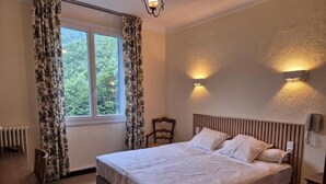 A bedroom with a bed, a desk, a chair, a window with curtains, and wall-mounted lights. - Hotel Val Du Tech  (Prats-de-Mollo-la-Preste)