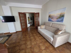 Ein Wohnzimmer mit einem beigefarbenen Sofa, einem an der Wand montierten Flachbildfernseher und einem hexagonal gemusterten Boden.