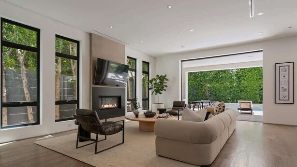 A spacious living room with a fireplace, large windows, and a view of greenery outside. - Villa Croft | Beverly Hills Luxury Hideaway (Los Angeles)