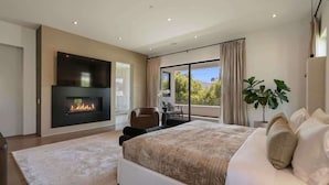 A modern bedroom with a fireplace, a large bed, a balcony with a view, and a dining area. - Villa Croft | Beverly Hills Luxury Hideaway (Los Angeles)