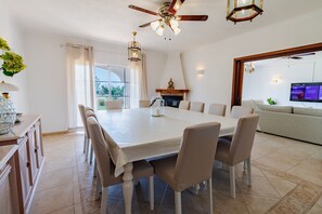 Ein Essbereich mit großem Tisch, Stühlen, Deckenventilator und Kamin.