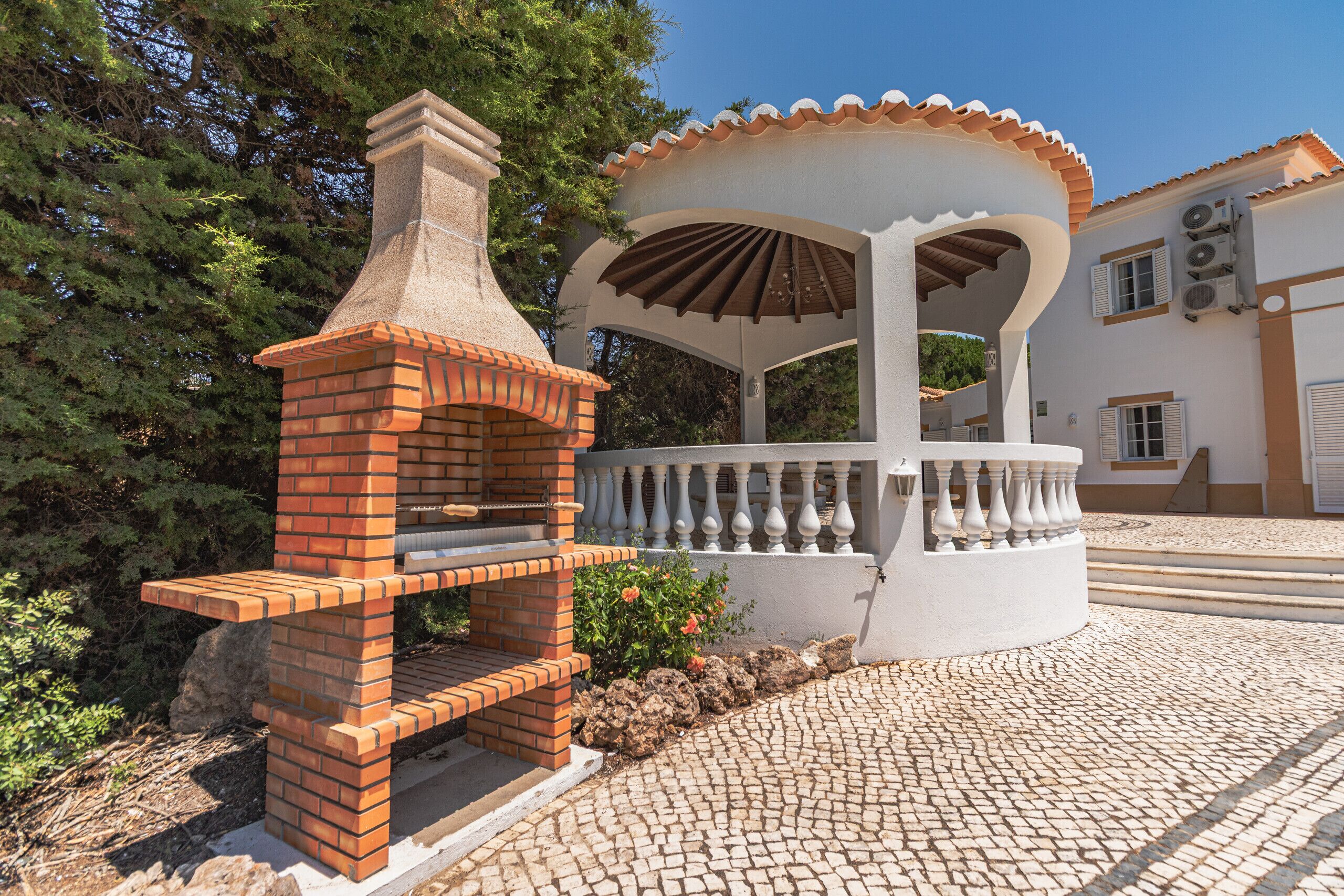 Un barbecue extérieur en briques, un gazebo blanc avec un toit en tuiles et un chemin pavé de pierres.