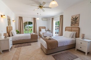 A hotel room with two beds, a ceiling fan, a window with curtains, a bedside table with a lamp, and a wall-mounted air conditioner. - Villa Paraiso | 6 bedrooms | Jacuzzi | Carvoeiro (Carvoeiro)