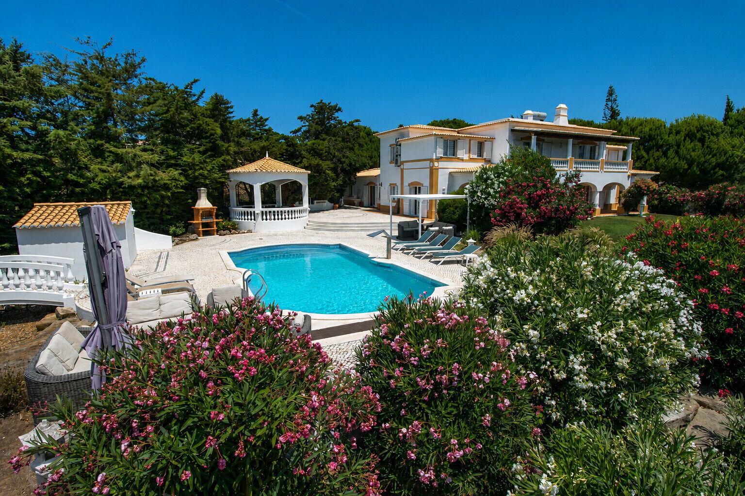 A pool with lounge chairs, a gazebo, and a large house with a garden.