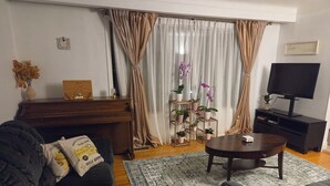 Ein Wohnzimmer mit einem dunklen Sofa, einem Couchtisch, einer TV-Konsole, einem Klavier und einem Pflanzenständer.