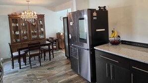 Eine Küche mit Esstisch, Stühlen, einer Pendelleuchte, einem Kühlschrank und einem Schrank.