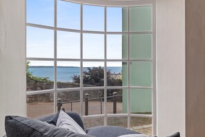 A room with a large bay window overlooking a coastal area, a stone wall, and a paved walkway. - Tenby Harbour View - Heart of Tenby, Sea Views (Tenby)