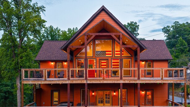 A two-story log cabin with a balcony, large windows, and a stone foundation. - Gorgeous 4-bedroom cabin with Views Overlooking Walking Distance to Gatlinburg (Gatlinburg)