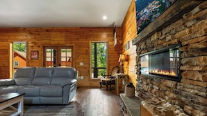 A cozy cabin interior with a stone fireplace, a leather sofa, and a wooden dining table. - Gorgeous 4-bedroom cabin with Views Overlooking Walking Distance to Gatlinburg (Gatlinburg)
