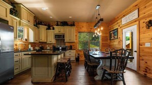 A cabin-style kitchen with wooden walls, a central island, and a dining area with wooden chairs. - Gorgeous 4-bedroom cabin with Views Overlooking Walking Distance to Gatlinburg (Gatlinburg)
