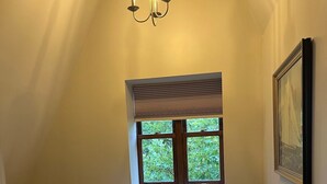 A bedroom with a bed, a window, a picture on the wall, and a chandelier.