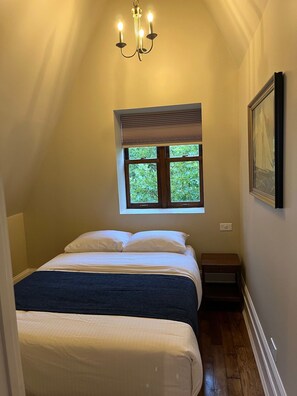 Un dormitorio con una cama, una ventana, un cuadro en la pared y un candelabro.