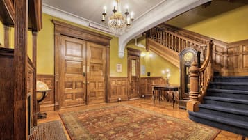 Un vestíbulo imponente con una amplia escalera de madera, un candelabro y piso alfombrado.
