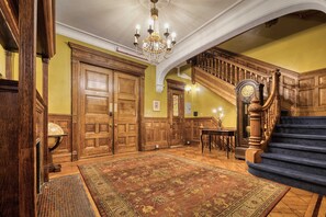 A grand foyer with a large wooden staircase, a chandelier, and a carpeted floor.