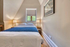 A bedroom with a bed, two bedside lamps, a window with blinds, and a framed picture on the wall. - Hamilton House Apt 7 with Pvt Bathroom (New York)