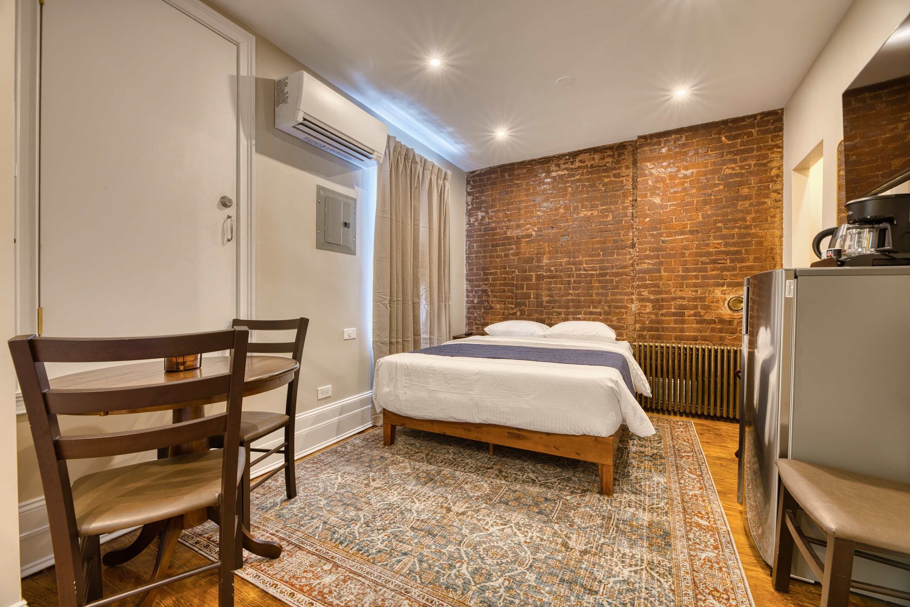 Ein Schlafzimmer mit Backsteinwand, einem Bett mit weißer Bettwäsche, einem Holzstuhl, einem kleinen Tisch und einem Heizkörper.