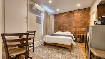 Ein Schlafzimmer mit Backsteinwand, einem Bett mit weißer Bettwäsche, einem Holzstuhl, einem kleinen Tisch und einem Heizkörper.