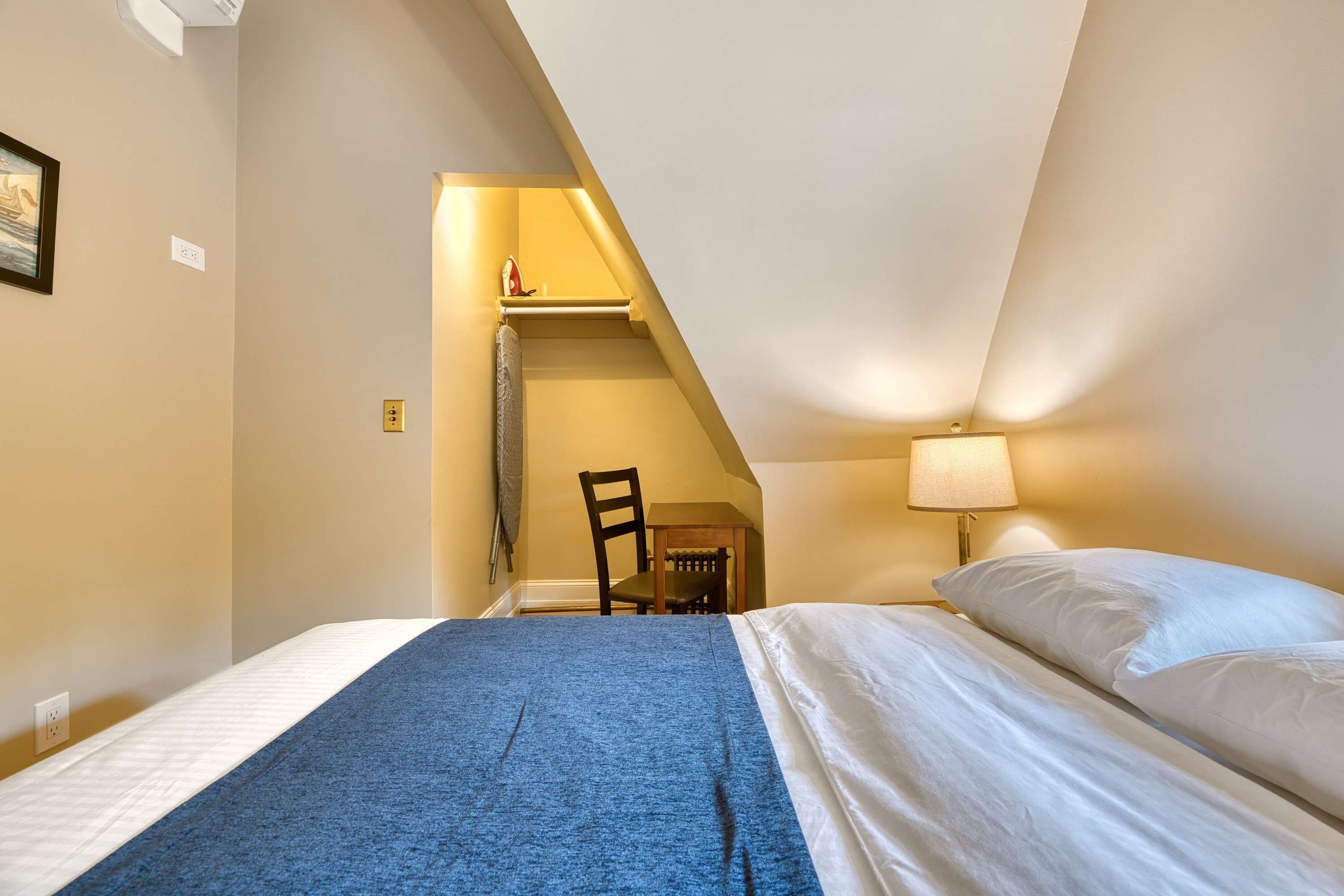 Ein Schlafzimmer mit Bett, Stuhl, Schreibtisch und Lampe.