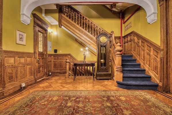 A grand staircase with a wooden handrail and blue carpeted steps, leading to an upper floor.