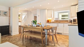 A modern kitchen with a wooden dining table, white cabinets, and a herringbone floor pattern. - Rose Cottage - Sea Views, Hot Tub, Log Burner (Pendine)