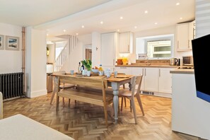 A modern kitchen with a wooden dining table, white cabinets, and a herringbone floor pattern. - Rose Cottage - Sea Views, Hot Tub, Log Burner (Pendine)