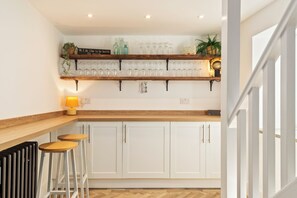 A kitchen with wooden countertops, white cabinets, and a shelf with glassware. - Rose Cottage - Sea Views, Hot Tub, Log Burner (Pendine)