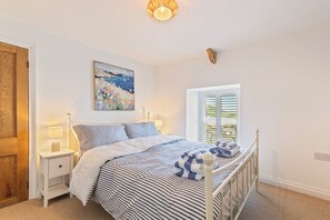 A bedroom with a bed, bedside tables, a window, and a painting on the wall. - Rose Cottage - Sea Views, Hot Tub, Log Burner (Pendine)