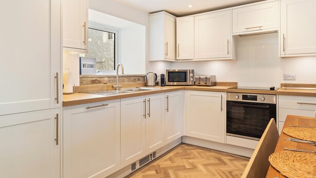 A modern kitchen with white cabinets, a microwave, toaster, and oven. - Rose Cottage - Sea Views, Hot Tub, Log Burner (Pendine)