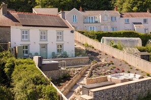 A residential area with a stone retaining wall, a garden with various plants, and a white house with a sloped roof. - Rose Cottage - Sea Views, Hot Tub, Log Burner (Pendine)