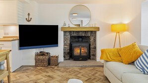 A living room with a fireplace, a television, a sofa, and a lamp. - Rose Cottage - Sea Views, Hot Tub, Log Burner (Pendine)
