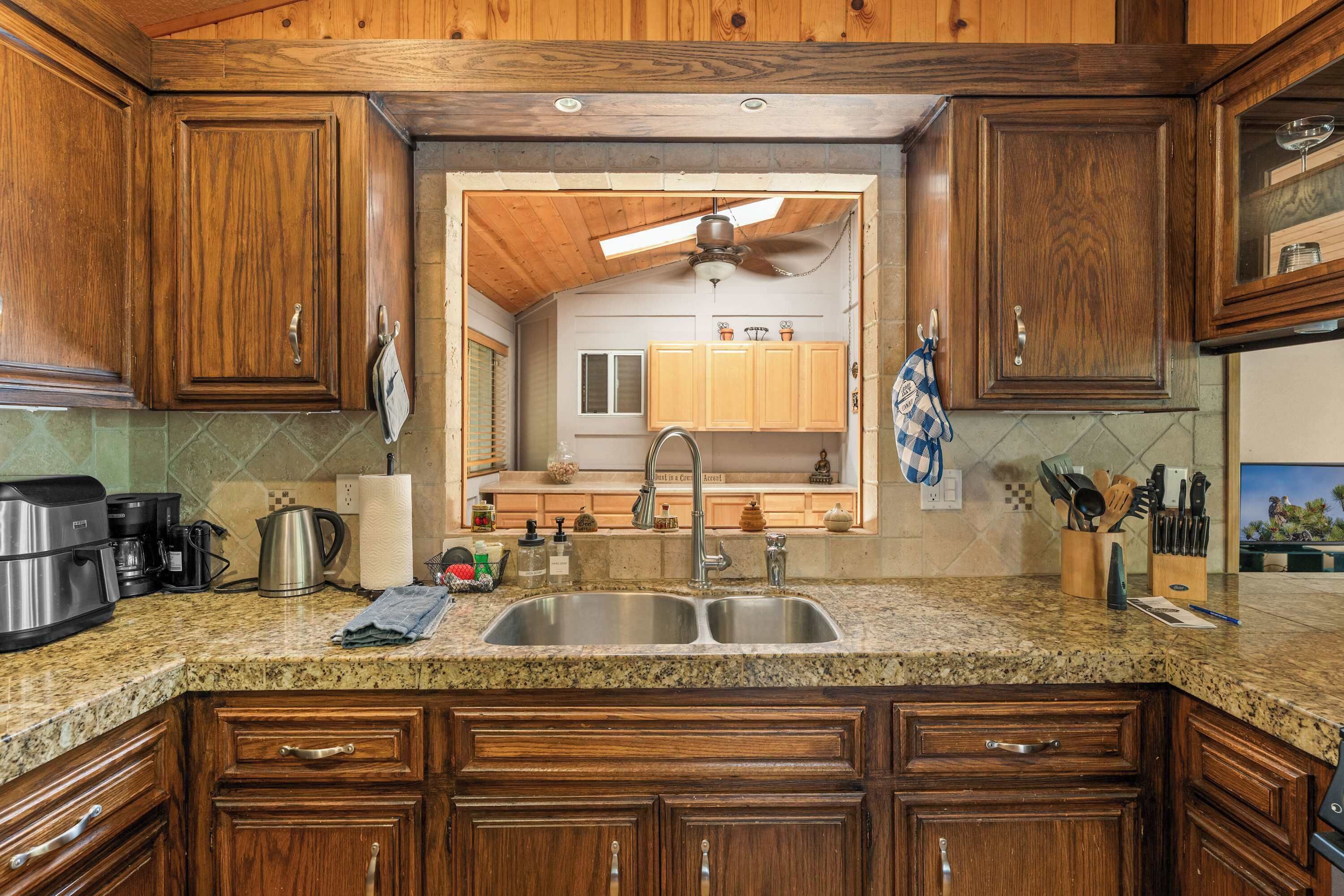 A kitchen with wooden cabinets, granite countertops, a double sink, and a ceiling fan.