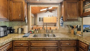 A kitchen with wooden cabinets, granite countertops, a double sink, and a ceiling fan. - Walk to Snow Summit, AC, Fenced Yard (Big Bear Lake)